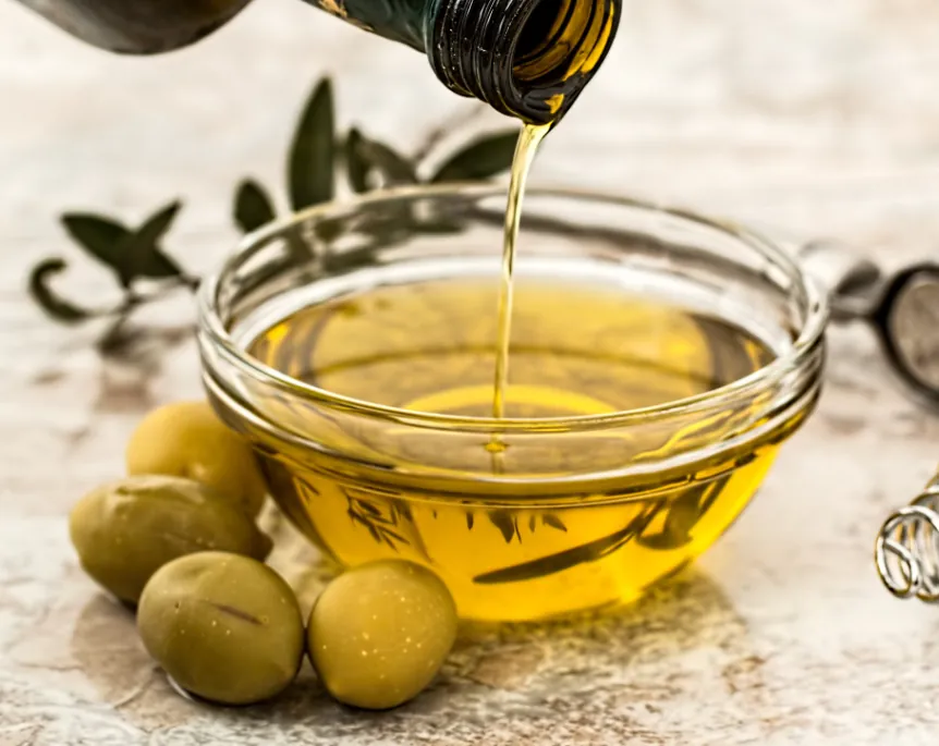 Olio extravergine versato in una ciotola di vetro, con olive verdi
